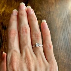 a woman's hand with a diamond ring on top of her left hand, against a wooden table