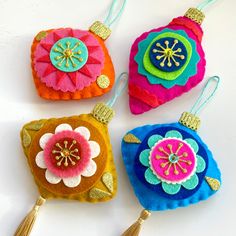 four colorful ornaments with tassels hanging from them on a white surface, one has a flower in the center