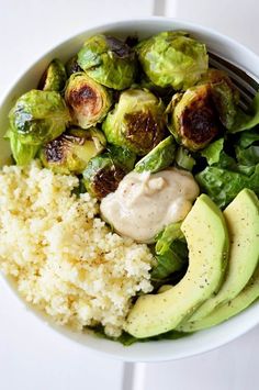 a white bowl filled with rice, brussel sprouts and avocados