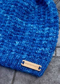 a blue knitted hat with a wooden tag on the front and back of it