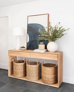 a wooden table with baskets on it next to a lamp and a framed painting in the background