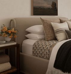 a bed with pillows and blankets on top of it next to a painting hanging above the headboard