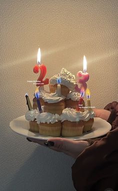 a person holding a plate with cupcakes on it and candles in the middle