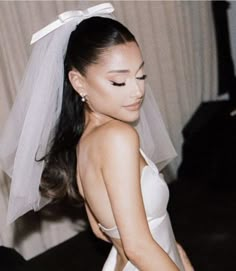 a woman wearing a white wedding dress and veil with her hair in a pony tail