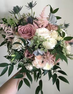 a bouquet of flowers is being held up by someone's hand in front of a white wall