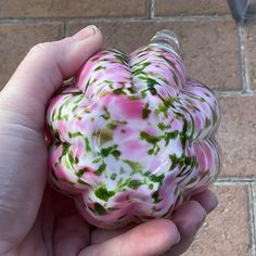 a hand holding a pink and green heart shaped object on top of a brick floor