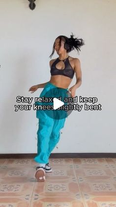 a woman is dancing on the floor with her hands in her pockets and wearing blue pants