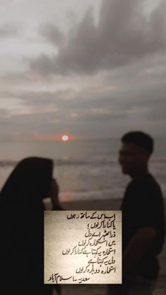 a man and woman sitting on the beach next to each other looking at the ocean