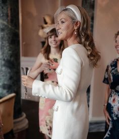 a woman in a white coat and hat holding a wine glass with two other women standing behind her