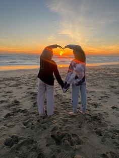 two women holding hands on the beach at sunset with their faces in the shape of a heart