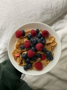 a white bowl filled with cereal and berries on top of a person's hand