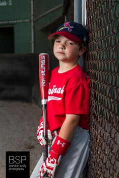 a young boy holding a baseball bat leaning against a fence