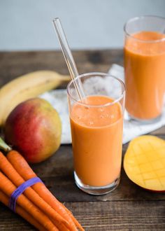 two glasses filled with orange juice next to some fruit and vegetables on a wooden table