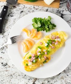 an omelet with ham and vegetables on a white plate next to a fork