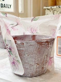 an old bucket sitting on top of a table covered in white paper and pink flowers