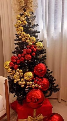 a small christmas tree with red and gold ornaments on it's top, sitting in front of a window