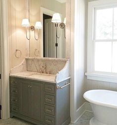 a bathroom with a tub, sink and mirror next to a bathtub in front of a window