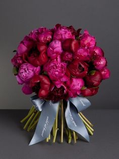 a bouquet of pink and red flowers on a gray background with a blue ribbon tied around it