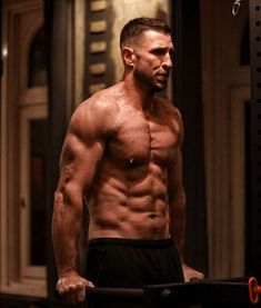 a shirtless man standing in the middle of a gym with his hands behind his back