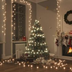 a christmas tree is lit up in front of a fireplace with presents on the floor