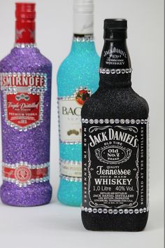 three bottles of jack daniels are lined up on a white surface, one is blue and the other is red