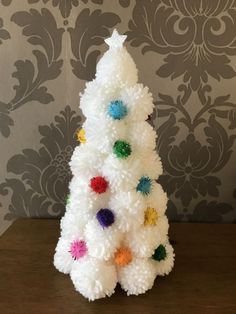 a white christmas tree with multi colored pom - poms on it's base