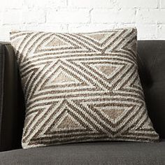 a brown and white pillow sitting on top of a gray couch next to a brick wall