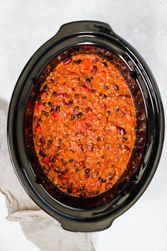 a crock pot filled with chili and beans on top of a white table cloth