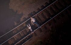 two people standing on train tracks in the middle of an aerial view, with their arms around each other