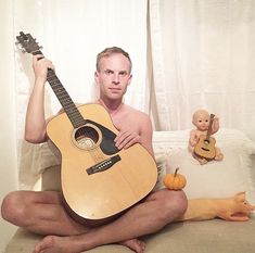 a man sitting on a couch with a guitar in front of him and a doll behind him