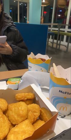 a woman sitting at a table with some food in front of her and a cell phone