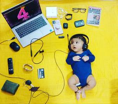 a baby wearing headphones sitting in front of a laptop computer on a yellow blanket