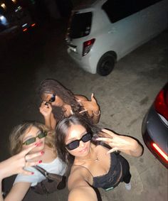 three young women standing next to each other in front of a car