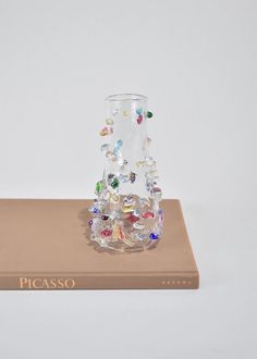 a small glass vase sitting on top of a brown book with colorful beads in it