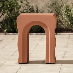 an orange sculpture sitting on top of a brick floor next to a plant filled area