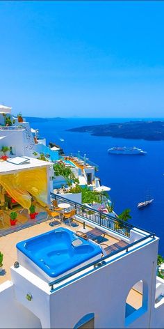 an outdoor swimming pool on top of a white building with blue water and boats in the background