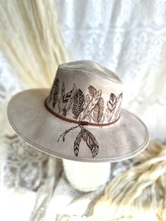 The feathers on this tan, faux suede hat are hand burned to create a stylish piece that would be perfect as a lovely boho/western statement piece.   The hat is size SM/Medium with braided cord and  inner strings for a size adjustment. Burned Straw Hat, Felt Burning, Hat Burning Ideas, Hat Decorating Ideas, Painting Hats, Painted Apparel, Burn Hats, Burning Hats, Burnt Hat