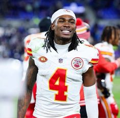 a man with dreadlocks standing on the sidelines wearing a football uniform and smiling