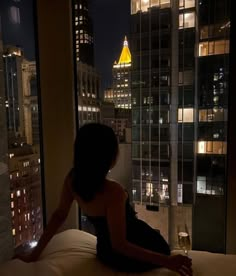 a woman sitting on top of a bed in front of a window with city lights