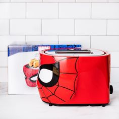 a red toaster sitting on top of a counter next to a spiderman poster