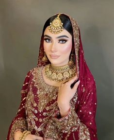 a woman in a red and gold bridal outfit with her hands on her chest