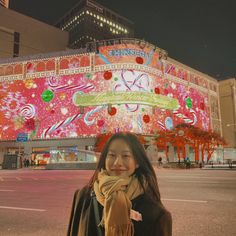 a woman standing in front of a large building with lights on it's side