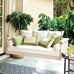 a white porch swing with green pillows and plants on the back wall, in front of an open patio door