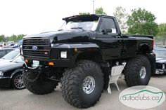 a large black truck parked in a parking lot next to other cars and trucks on display