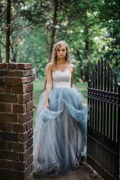 a woman standing in front of a black fence wearing a blue and white wedding dress