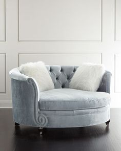 a blue chair with two white pillows on it and a wooden floor in front of a wall