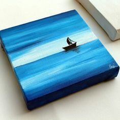 a painting of a small boat floating in the ocean on a white surface next to a book