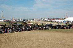 a large group of people standing in front of some old cars and trucks on a dirt field