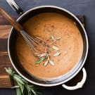 a pot filled with sauce and whisk on top of a wooden cutting board