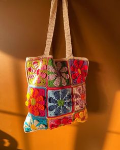 a multicolored crocheted bag hanging from a hook on a wall in the sunlight